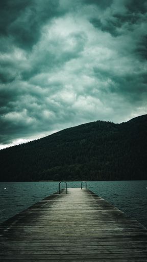 A beautiful view of a wooden pier and a mountain under the cloudy sky