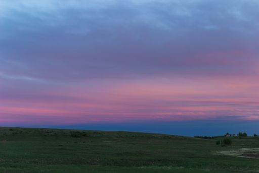 A beautiful view of a green field under the cloudy sky during a pink sunset