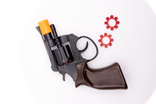 A closeup shot of a toy pistol revolver with its ammo against a white background