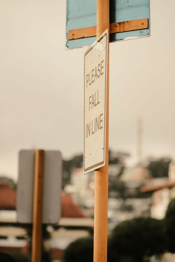 A vertical closeup of a road sign with "please fall in line" inscription