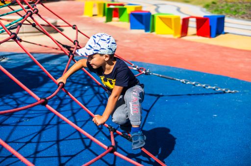 Young boy with a Batman shirt climbing on a rope equipment at a playground in the Rataje park.