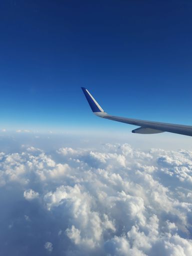 A vertical shot of a plane wing over the clouds in blue sky