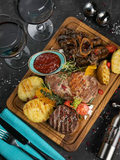 A top view of grilled meat and potatoes set with sauce on black wooden background