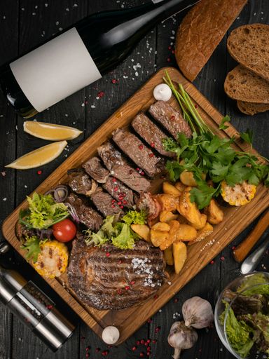 A top view of grilled meat and potatoes set with sauce on black wooden background