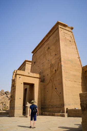 A low angle shot of a male standing in front of Isis Aswan Temple in Egypt