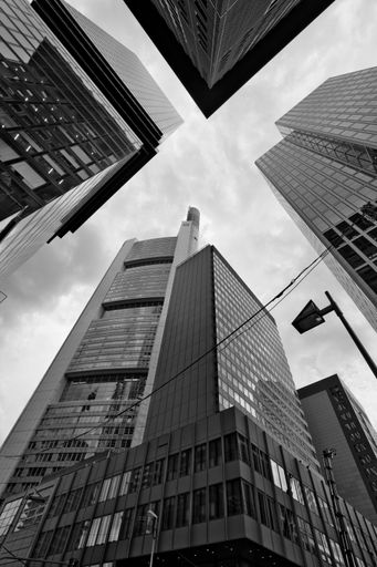 A low-angle shot of tall skyscrapers in the city of Frankfurt, in grayscale, with a cloudy sky in the background