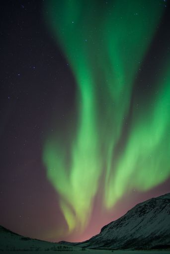 A vertical shot of bright green aurora northern lights over mountains in Norway