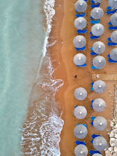 A scenic top view of a sand beach with umbrellas and the waves hitting the shore
