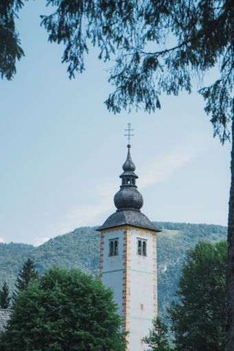 A vertical shot of Slovenian church with lush green mountains in the background