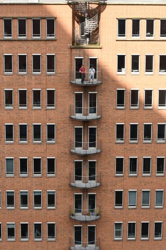 The vertical view of two men standing on the balcony of a brick-built building