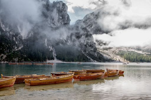 A scenic view of wooden boats moored in a lake against mountains covered with fog