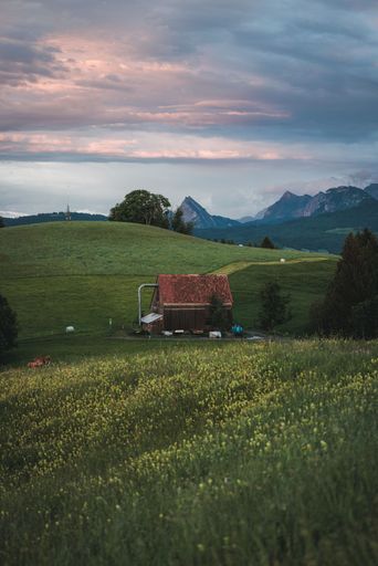 A vertical shot of countryside house in green field with mountains and cloudy sky in the background