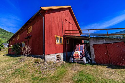 A wooden painted red house in the countryside with a tractor