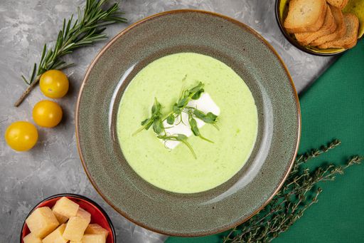 A close-up of a bowl of flavorful spinach cream soup, with crunchy cheese crackers