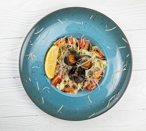 A delicious plate of pasta with clams and a lemon wedge, served against a white background
