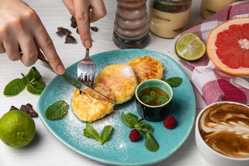 A close-up of a person using a kitchen knife to cut  pancakes on a blue plate
