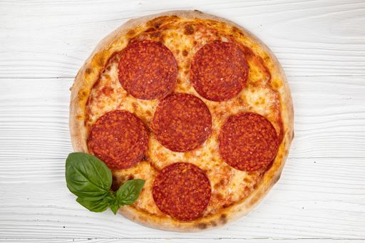 A freshly made pepperoni pizza served with a basil on a wooden table