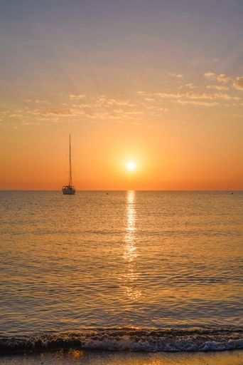 A vertical shot of the sea with a sailboat against the beautiful background of the sky at sunset.