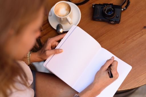 A high angle shot of a female writing in a notebook and drinking coffee