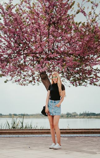 A vertical shot of a beautiful young lady posing in front of a flowering tree
