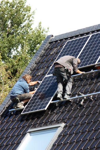 A vertical shot of construction workers installing solar panels to a roof