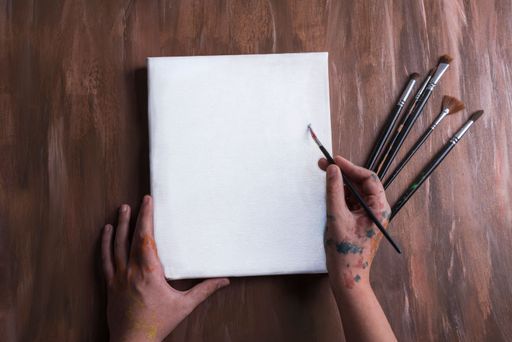 hand holding paintbrush, blank canvas on wooden table
