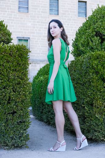 A vertical shot of the young woman with a green dress looking at camera and standing around plants
