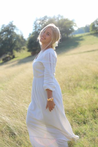 A female model wearing a flowing white dress standing in lush green field