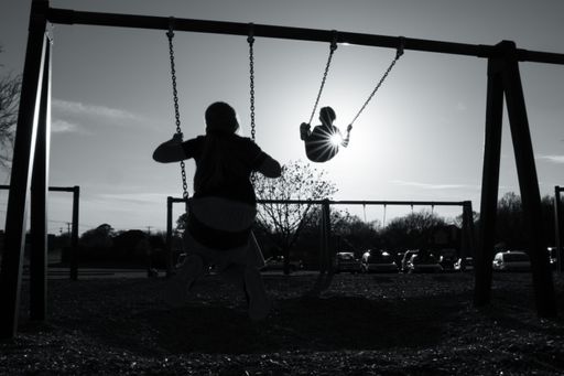 A grayscale shot of the mother with her child on the swings.
