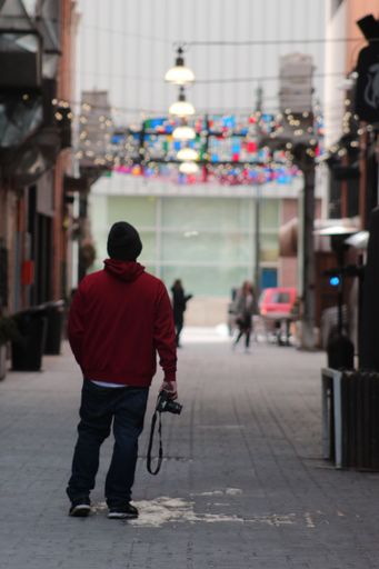 A vertical shot of a man with a camera in a red hoodie standing in the middle of the street