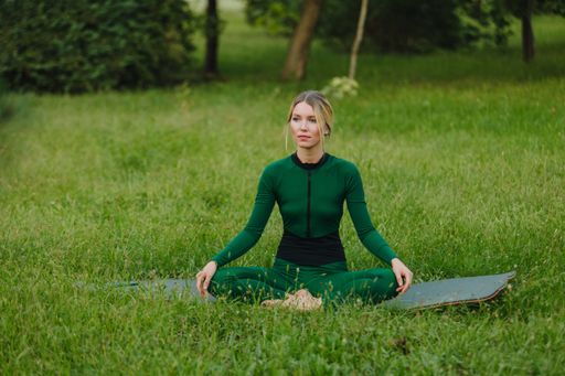 A young female practicing yoga asanas in the morning on green grass in the park