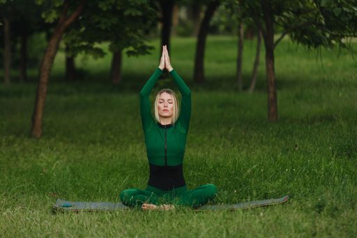 A young female practicing yoga asanas in the morning on green grass in the park