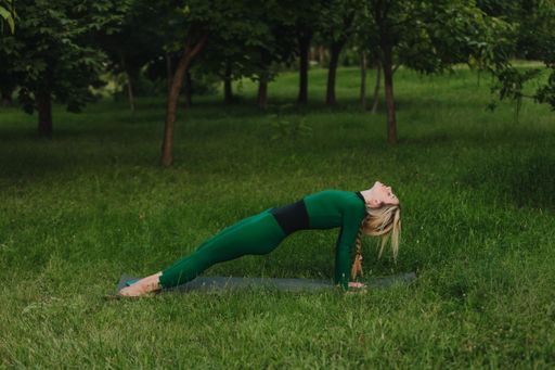 A young female practicing yoga asanas in the morning on green grass in the park