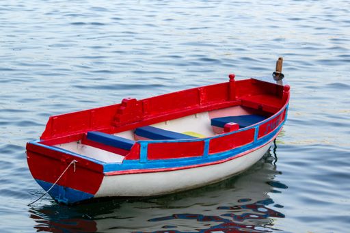 A small empty red boat on the wavy water