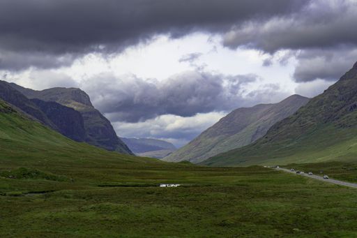 A scenic view of a road against a green mountain on a cloudy day in Scottish highlands
