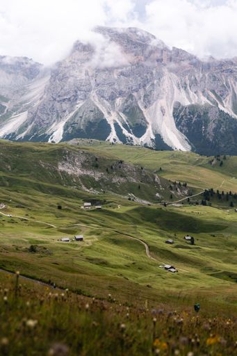 A vertical shot of rural houses on slope of green Dolomites mountains covered with clouds in Italy