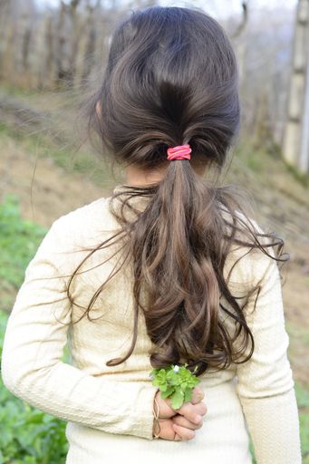A vertical shot of a cute girl with long hair holding a small flower behind her back