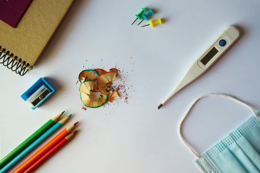 A high angle shot of school supplies, a medical mask, and a thermometer on a white surface - back to school concept in the new normal after Covid-19