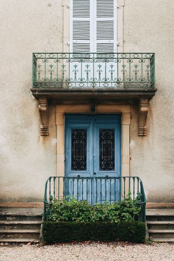 A vertical shot of an old building, blue entrance door and small balcony above it