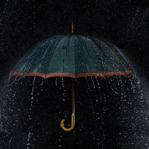 A closeup shot of umbrella under raindrops with black background
