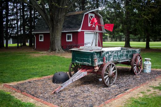An old green wooden wagon cart standing in front of a red barn in a rural area