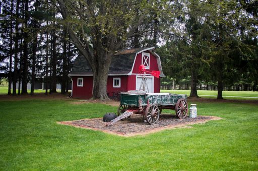 An old green wooden wagon cart standing in front of a red barn in a rural area