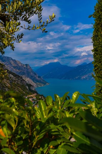 A vertical shot of a lake surrounded by hills and green plants on a sunny and cloudy day