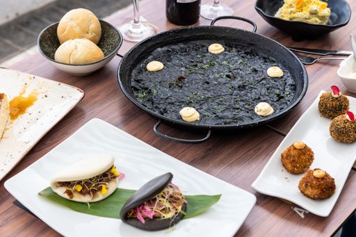A top view of Arros negre and variety of delicious dishes and cutlery on a wooden restaurant table