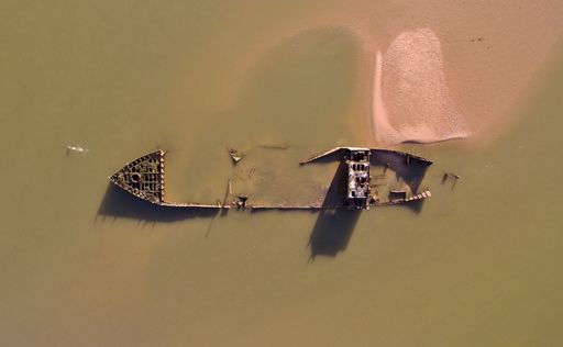 An aerial drone view of a sunken abandoned ship in a dirty water