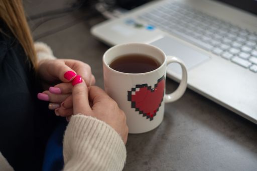 A closeup shot of the woman's hands near the pixel heart mug and a laptop