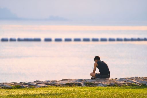A back view of human sitting on rock near lake