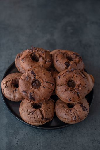 A top view of tasty chocolate donuts on black plate on gray background