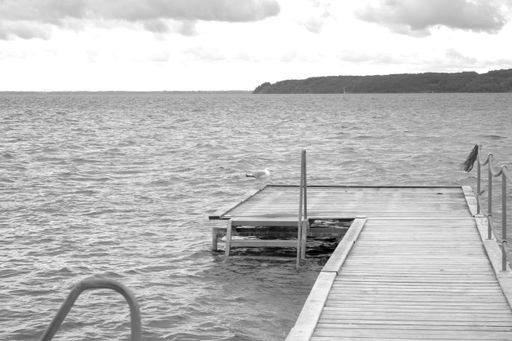A grayscale shot of a wooden dock near the beautiful sea under the cloudy sky