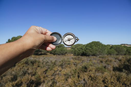 A closeup shot of a person's hand holding a compass with a field in the background